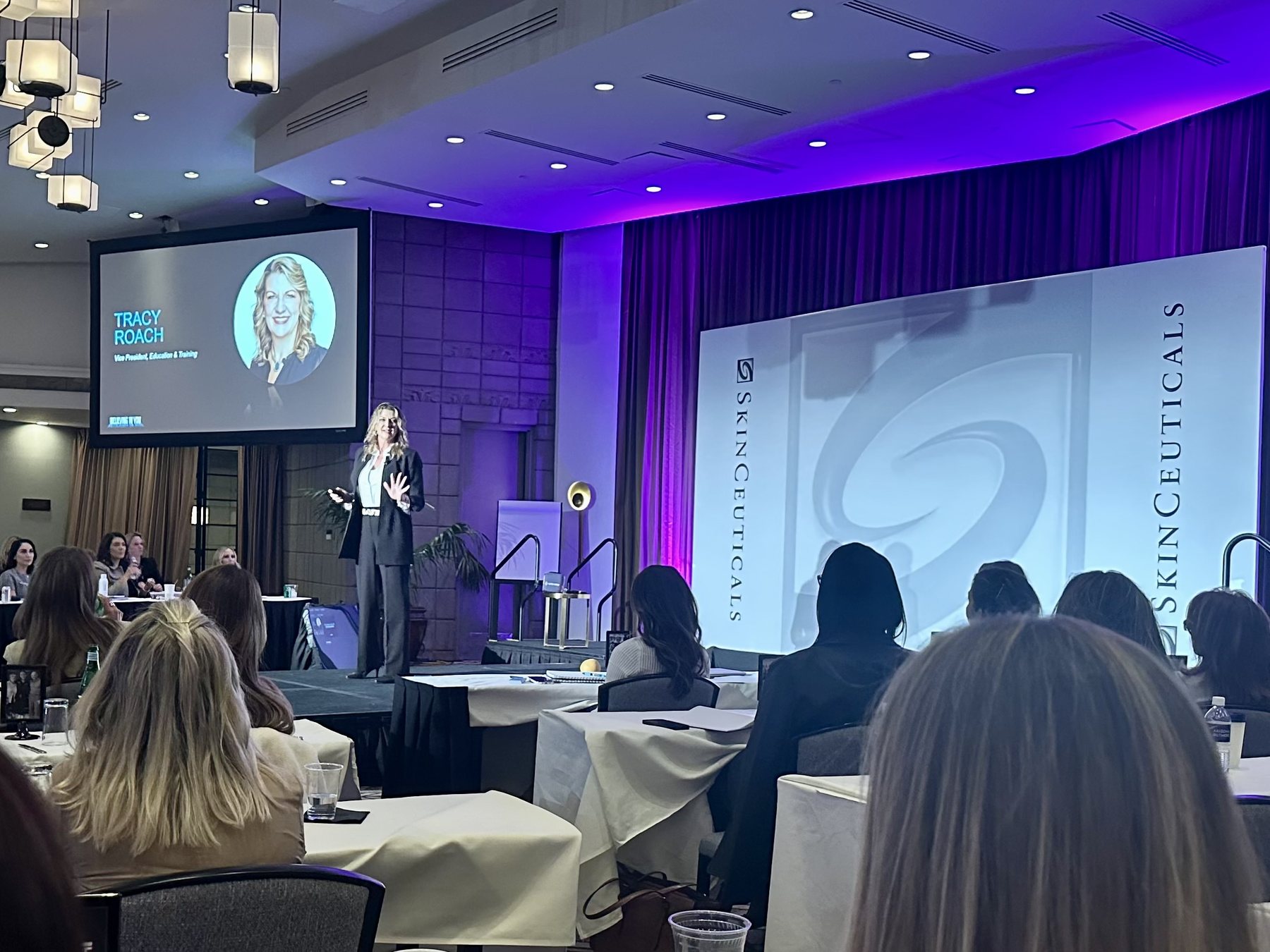 Tracy Roach presenting on stage at a SkinCeuticals training event